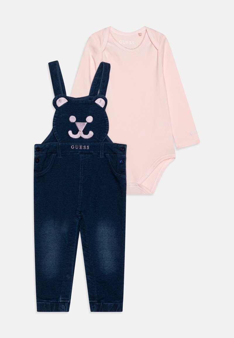 Body bébé rose à manches longues associé à une salopette bleu foncé avec un motif visage d'ours et le logo "GUESS" sur le devant.