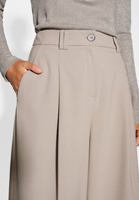 Beige high-waisted broeken met een knoopsluiting, voorzien van een gladde textuur, zijzakken en scherpe voorplooien.