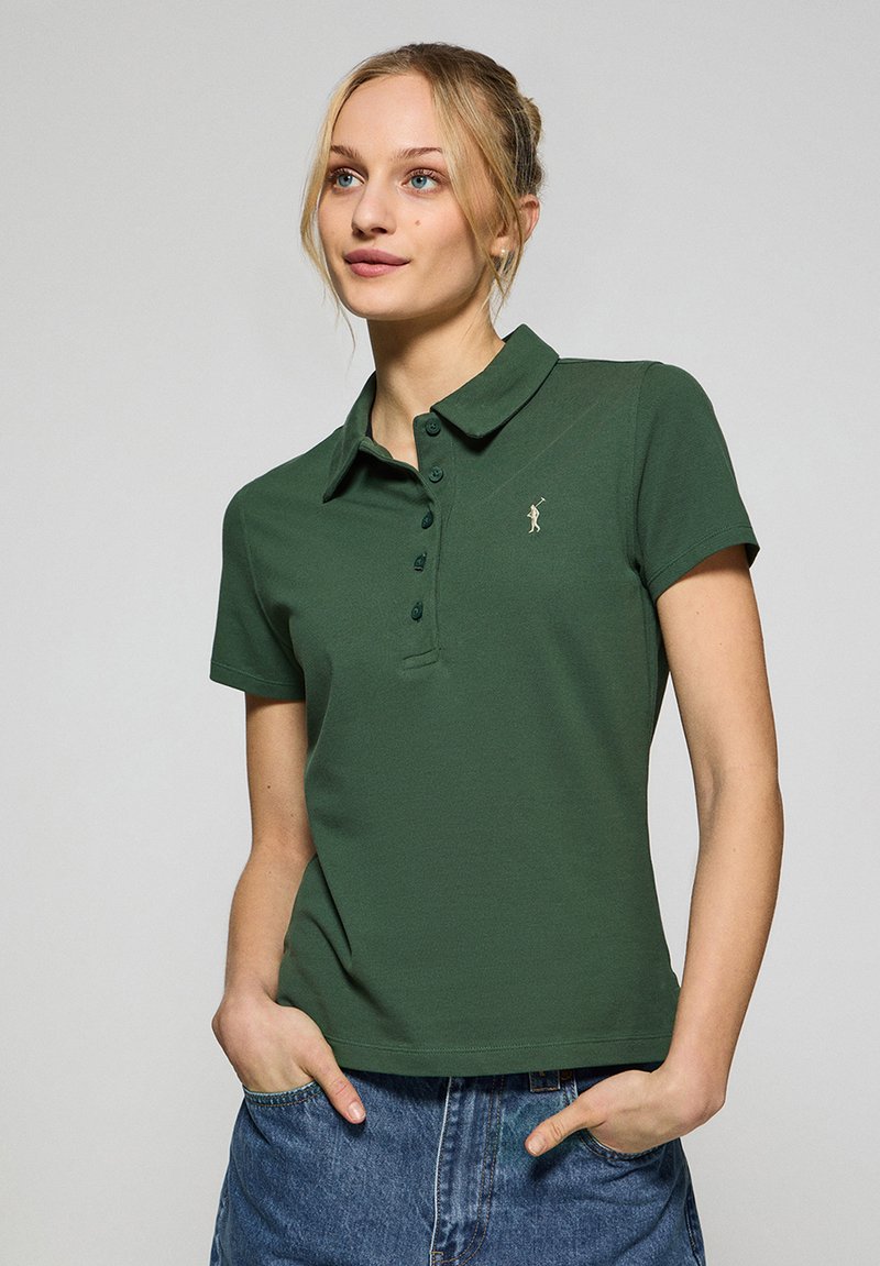 Zielona koszulka polo wykonana z bawełny, z klasycznym kołnierzykiem, guzikową listwą i małym emblematem na lewej piersi. Krótkie rękawy.