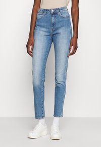 Höga ljusblå denimjeans med en blekt finish, fem-fickorsdesign och smal passform; kombinerade med vita sneakers och ankelsockor.