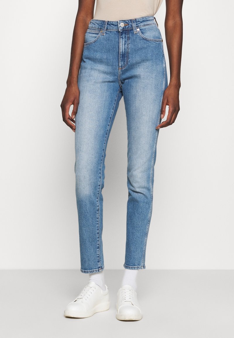 Höga ljusblå denimjeans med en blekt finish, fem-fickorsdesign och smal passform; kombinerade med vita sneakers och ankelsockor.