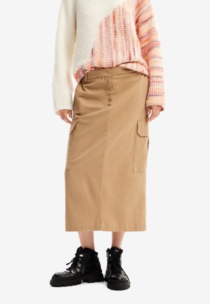 Beige knee-length skirt with cargo pockets, made of cotton. Worn with a multicolored knitted sweater and black lace-up boots.
