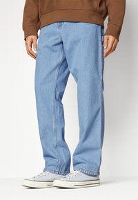 Hellblaue Denim-Jeans mit einer lockeren Passform, ausgestattet mit Seitentaschen, einem geraden Schnitt und kontrastierenden Nähten. Getragen mit grauen Leinen-Schuhen.