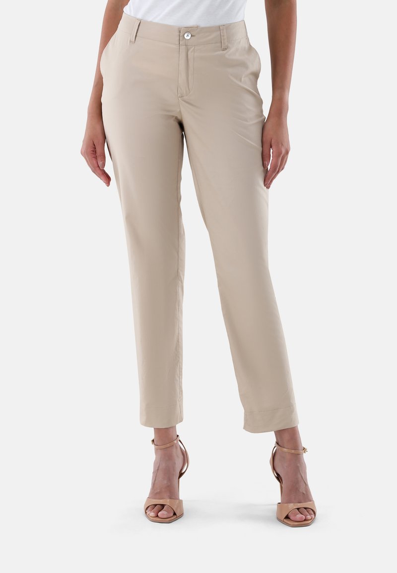 Beige Hosen mit maßgeschneidertem Schnitt, vorderen Taschen und einem Knopfverschluss. Glatte Stoffoberfläche mit leichtem Glanz. Kombiniert mit beigen Absatzschuhen.