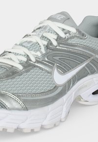 Ασημί και λευκό παπούτσι τρεξίματος Nike με επάνω μέρος από δίχτυ, επενδυμένη σόλα, λευκά κορδόνια και εμφανές λογότυπο Nike swoosh στο πλάι.