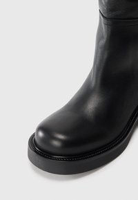 Zwarte leren enkelboot met een ronde neus, een gladde textuur en een dikke zool. Heeft een subtiele naaddetail langs de bovenrand.