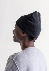 Gorro negro tejido con punta afilada, llevado sobre una sudadera gris. El gorro presenta una textura acanalada y un ajuste ceñido.