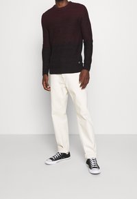 Bordeaux crewneck trui met gestructureerde brei, gecombineerd met lichtbeige recht-pas broek en zwarte lage sneakers.