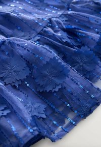 Tessuto di abito blu trasparente con applicazioni floreali e paillettes. Presenta strati testurizzati e strisce orizzontali di decorazioni.