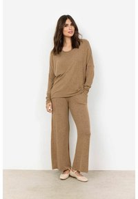 Rudas mezgimo loungewear komplektas, kuriame yra plačių apykaklės ilgomis rankovėmis marškiniai ir plačios kelnės. Tekstūruota medžiaga su laisvu siluetu. Šviesios spalvos butai.