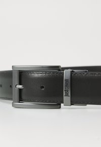Cinturón de cuero negro con hebilla de tono plateado cepillado, presenta ranuras verticales y un acento de logo. Textura suave y ajuste ajustable.
