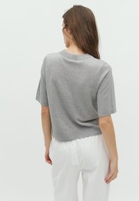 Pulover gri cu mânecă scurtă, guler rotund, design scurt, textură fină și tiv ribetat, purtat cu pantaloni albi ușori.