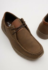 Zapatos de cuero marrón con una forma redondeada, detalles cosidos y un acento de cuero color beige. Cierre con cordones y suelas de goma para mayor tracción.