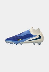 Chuteira de futebol azul e creme com uma parte superior texturizada, design de tornozelo ajustado e detalhes amarelos, apresentando tachas translúcidas na sola.