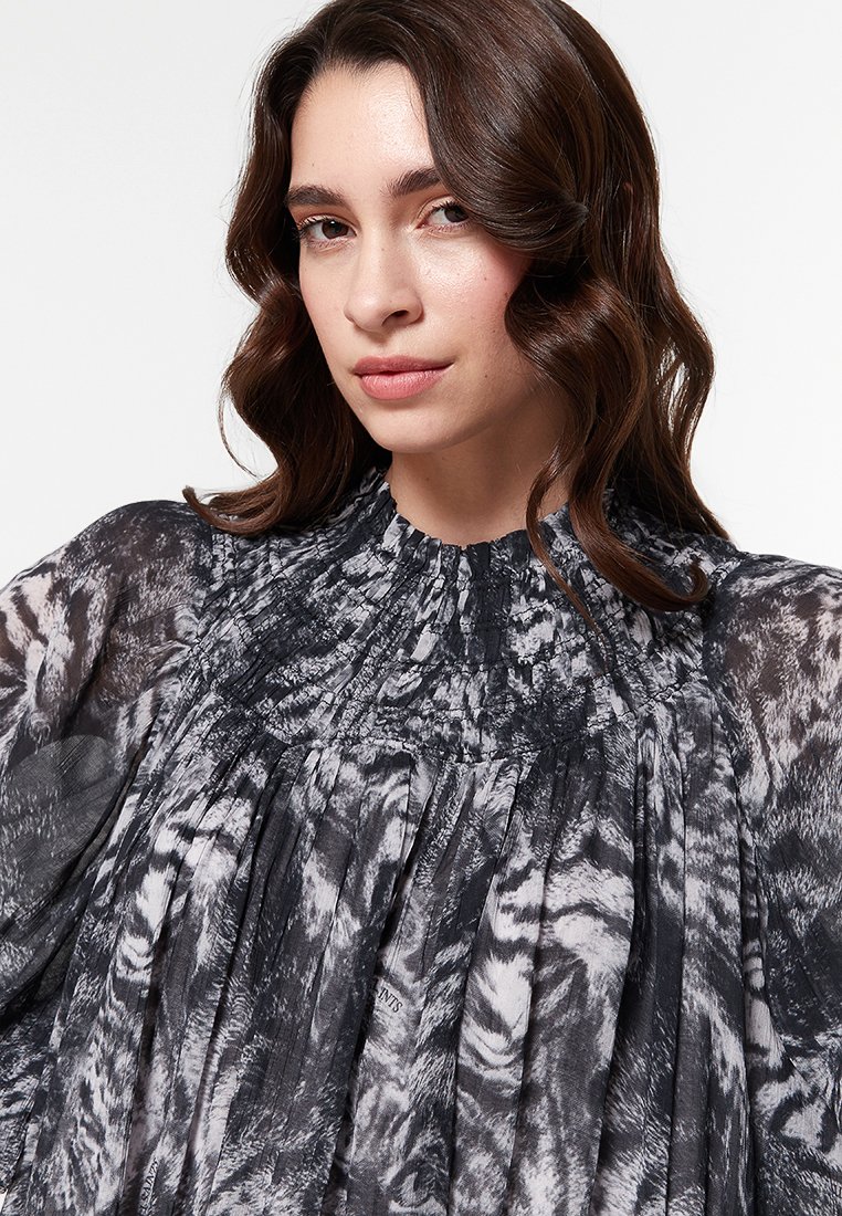 Zwart-witte blouse met een geplooid design, gathered halslijn en een doorschijnende, gestructureerde stof met abstracte patronen.