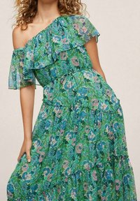 Green floral off-the-shoulder dress with ruffled sleeves, layered skirt, and tie detail, featuring a textured fabric with pink and blue patterns.