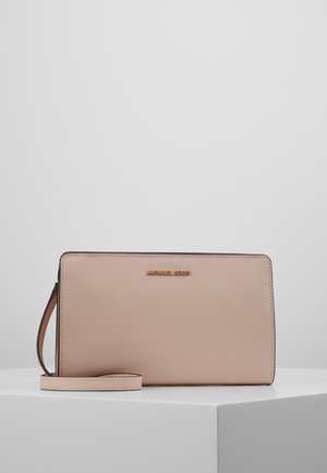 Rechthoekige beige polstas met een gestructureerd oppervlak, smalle band en een goudkleurig "Michael Kors"-logo aan de voorkant, geplaatst op een wit platform.
