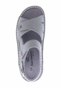 Grey suede sandal featuring an open design with crossed straps, decorative hardware, and stitched detailing along the edges. Comfort-focused design.