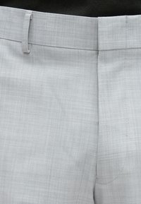 Šviesiai pilkos, specialiai pasiūtos kelnės su subtiliu languotu raštu. Lygus priekis, siaura juosmens juosta ir lygi audinio tekstūra.