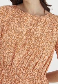 Pomarańczowa sukienka z teksturowanej tkaniny z białym abstrakcyjnym wzorem, o zaokrąglonym dekolcie i marszczonym pasie, zapewniająca dopasowany krój.