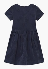 Námořnická modrá šaty s krátkým rukávem a nařasenou sukní, poseté vyšitými hvězdnými vzory, s uzavíráním na zip na zadní straně.