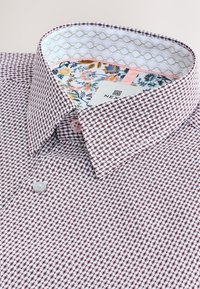 Chemise à manches courtes avec un motif à carreaux bordeaux et blanc, en tissu coton, avec un col intérieur à motif floral et des détails de boutons.