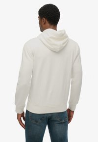 Sudadera de color beige claro con capucha ajustable, puños y dobladillo acanalados. Confeccionada en una tela suave, presenta un ajuste relajado y costuras en la parte trasera.