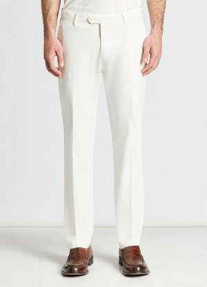 Uomo che indossa pantaloni bianchi su misura e mocassini in pelle marrone, in piedi davanti a uno sfondo semplice.