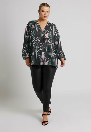Floral blouse in black, green, and purple tones, with long sleeves and a V-neck, paired with black fitted leggings and strappy black sandals.