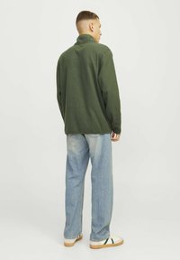 Pullover in pile verde con colletto alto, vestibilità morbida e maniche lunghe. Abbinato a jeans azzurri chiari e sneakers bianche. Design semplice.