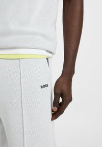Witte mesh sweatshirt met een ronde halslijn, gecombineerd met lichtgrijze perforerende sweatpants met een zwart "BOSS" logo op de zak.