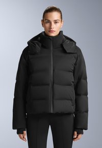 Crna puf jakna s visokim ovratnikom, zatvorenim patentnim zatvaračem sprijeda i oversized siluetom. Ima panele s punjenjem, odvojivu kapu i elastične manžete.