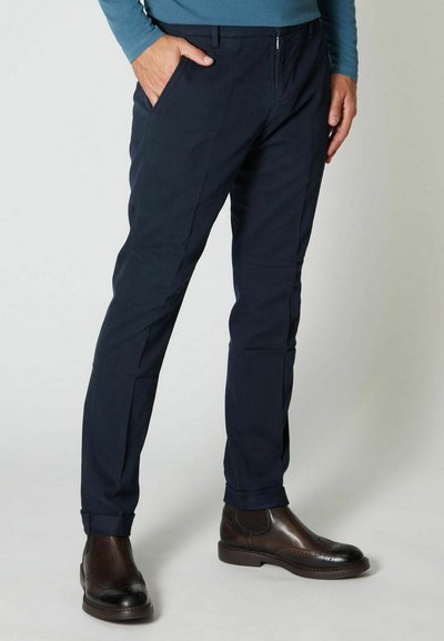 Pantaloni blu navy in tessuto leggero, dotati di zip, due tasche laterali e una vestibilità affusolata, abbinati a stivali in pelle marrone.