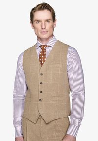 Beige Wollweste mit Karomuster, fünf Knöpfen und einer Vordertasche, kombiniert mit einem gestreiften lila-weißen Hemd und einer gepunkteten Krawatte.