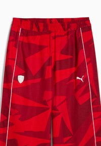 Rode sportieve broek met een hoekig geometrisch patroon, elastische tailleband en witte accenten met het Puma-logo en merkembleem.