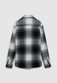 Chemise en flanelle à carreaux noirs et blancs, dotée de manches longues, d'un col avec revers et de poignets boutonnés. Texture douce avec un motif classique.