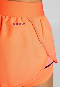Pantalones cortos atléticos ligeros en color naranja con un dobladillo curvado, que presentan un logotipo AEROREADY, cinturilla elástica y un forro en contraste en color rosa.