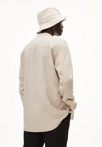 Beige linnen shirt met lange mouwen, knopenmanchetten en een gebogen zoom. Gecombineerd met een bijpassende beige bucket hat. Schone, minimalistische design.