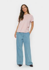 Svetlo roza majica s kratkimi rokavi, v kombinaciji s širokimi svetlo modrimi kavbojkami. Tkanina izgleda mehka, obleka pa je sproščena. Zgornji rjav čevlji.