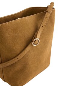 Brun ruskinds tote taske med en glat tekstur, der har en cirkulær metalaccent og en justerbar skulderrem, åben i toppen.