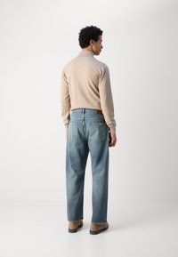 Beige strikkegenser med høy krage, sammen med lyseblå, avslappede jeans. Skoene er brune, ankelhøye med flat såle.