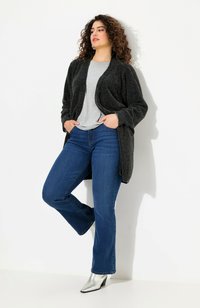 Musta teksturoitu kardigan harmaan paidan päällä, yhdistettynä sinisiin levennettyihin farkkusiin ja hopeisiin nilkkureihin. Kardiganissa on avoin etuosa.