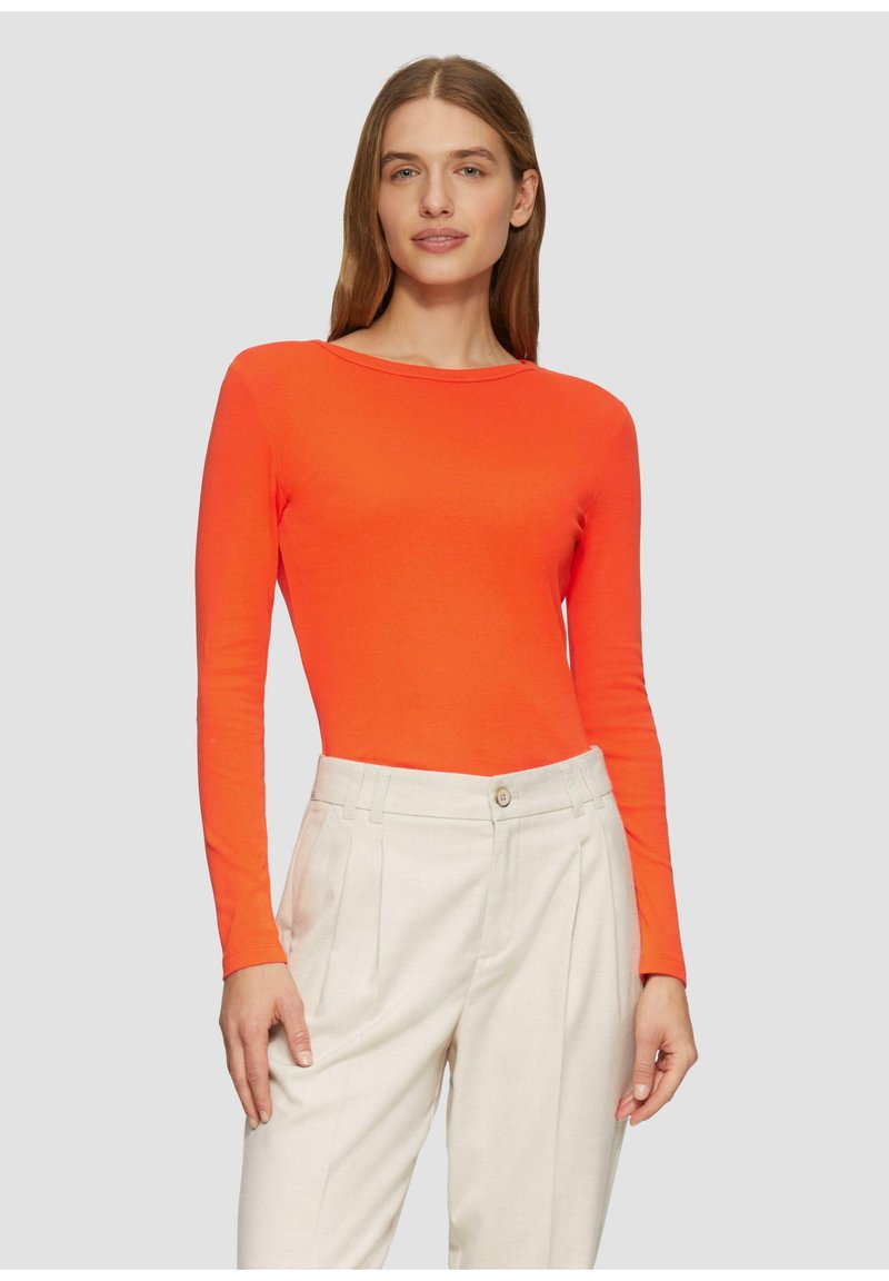 Langarmtop in feloranje stof met een bootnek. Gecombineerd met beige geplooide broek met een knoopsluiting.