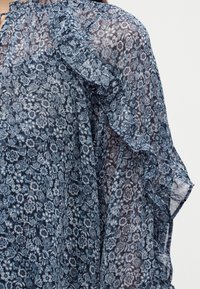 Διάφανη μπλε φλοράλ μπλούζα με βολάν στις ραφές και τα μανίκια, με σούρες στη λαιμόκοψη και ευαίσθητα λουλουδένια σχέδια παντού.