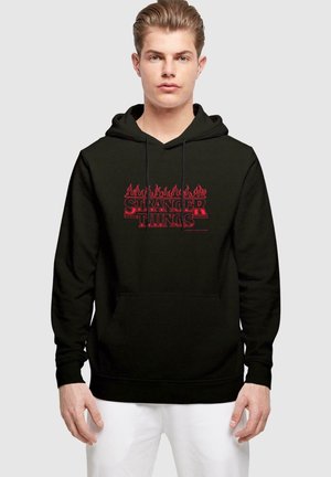 Black hooded sweatshirt with "STRANGER THINGS" logo in red flames on the front, featuring a kangaroo pocket and drawstring hood.