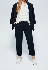 Granatowa marynarka na biało-paskowanej bluzce, zestawiona z ciemnymi, dopasowanymi spodniami i białymi tenisówkami; gładka tkanina, strukturalny fason, casualowy, a zarazem elegancki wygląd.