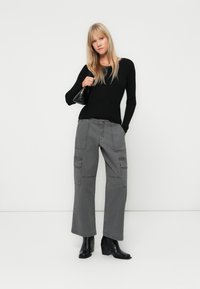 Pulover negru cu dungi, cu mânecă lungă, asortat cu pantaloni cargo gri, având buzunare laterale. Modelul poartă ghete negre până la gleznă, stând pe un fundal alb.