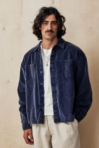 Cămașă din corduroy bleumarin cu butoni, echipată cu două buzunare pe piept și o croială ușor relaxată. Suprapusă peste un tricou alb, cu butoane vizibile.