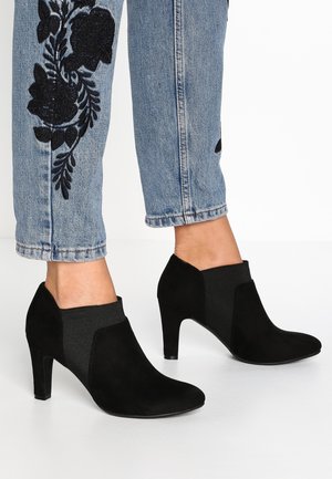 Stivaletti neri con tacco alto, caratterizzati da una finitura in suede e pannelli laterali elastici. Indossati con jeans ricamati color azzurro chiaro.