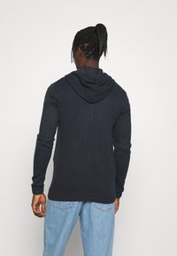 Felpa a maglia blu navy dal fit rilassato, con un ampio cappuccio e polsini a coste, abbinata a jeans in denim blu chiaro.